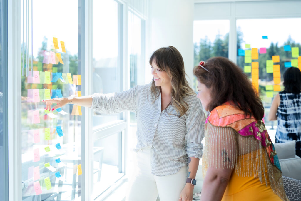 Two writers mapping chapters on a wall of sticky notes
